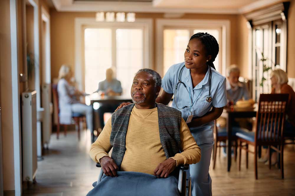 A senior man sitting in a wheelchair with a healthcare professional sitting behind him.